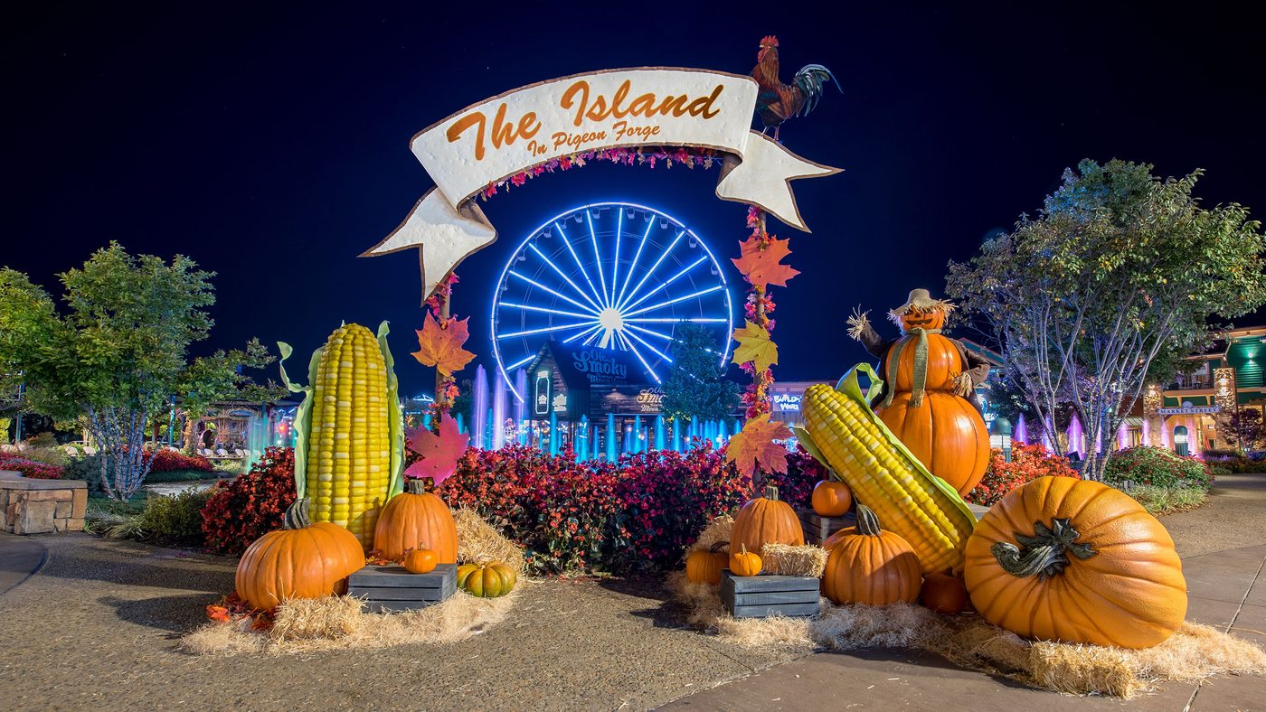 Night entrance arch at The Island in Pigeon Forge during Autumn's GLOW, with pumpkins, corn, and the Great Smoky Mountain Wheel.